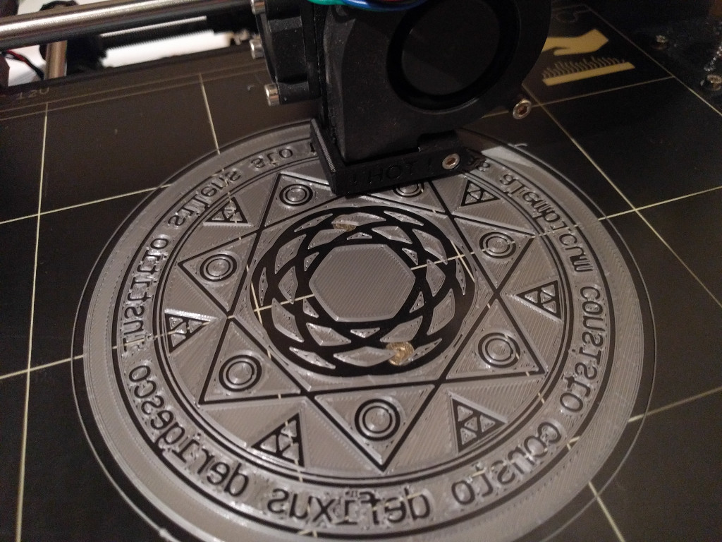 A magick circle composed of circles, triangles, latin text, a seven-pointed star, and a rose curve being printed on the bed of a 3d-printer.